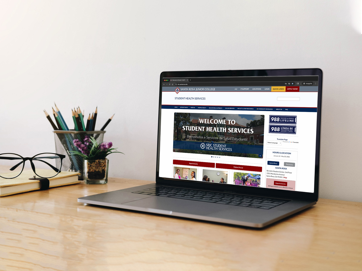 Laptop on a desk displaying a student health services webpage, with glasses and a pencil holder nearby.